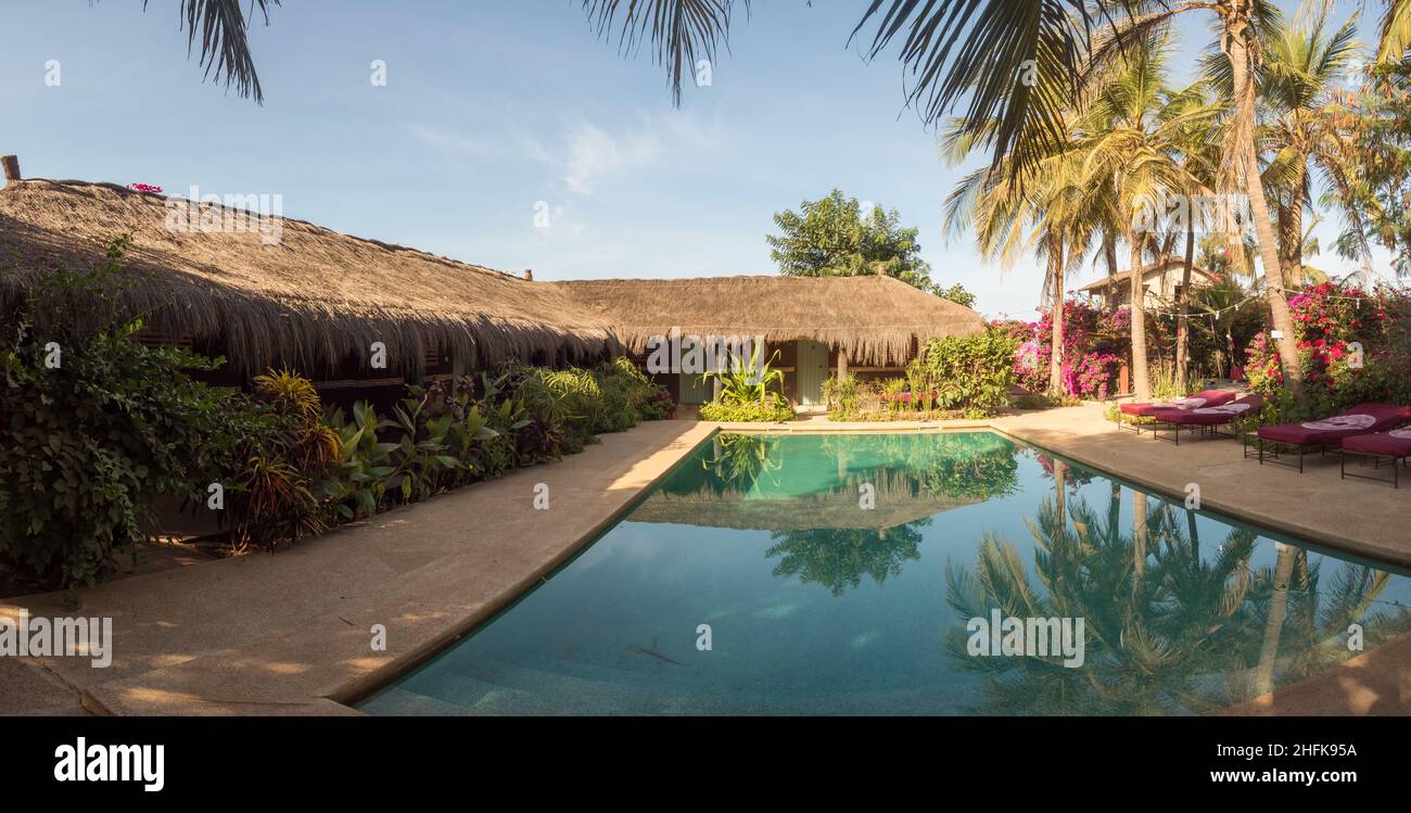 Senegal, Africa - Jan 2019: Table with tableware awaits guests and deck chairs covered with material in African colors around the pool and African hut Stock Photo