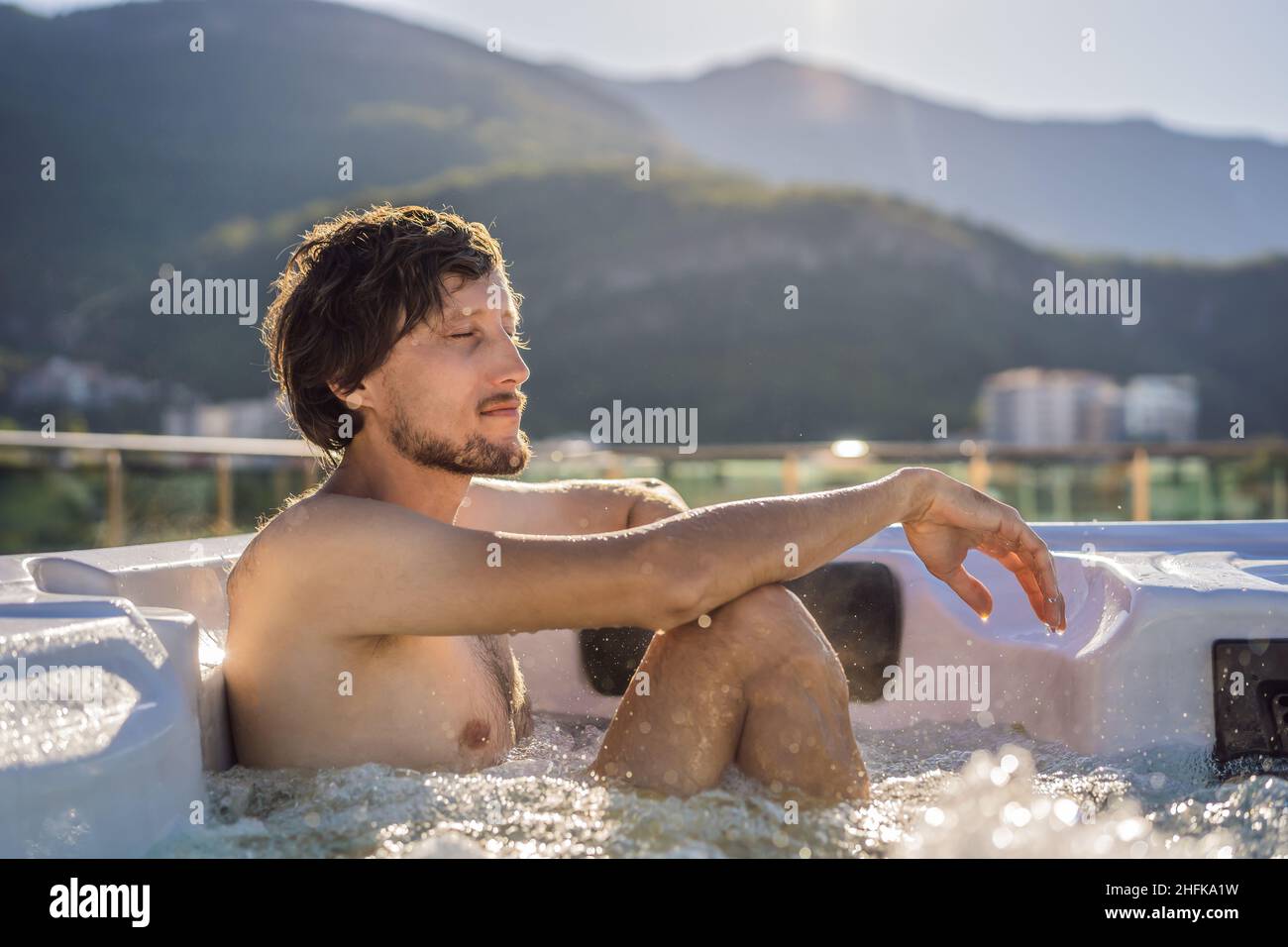Portrait of young carefree happy smiling man relaxing at hot tub during enjoying happy traveling moment vacation life against the background of green Stock Photo