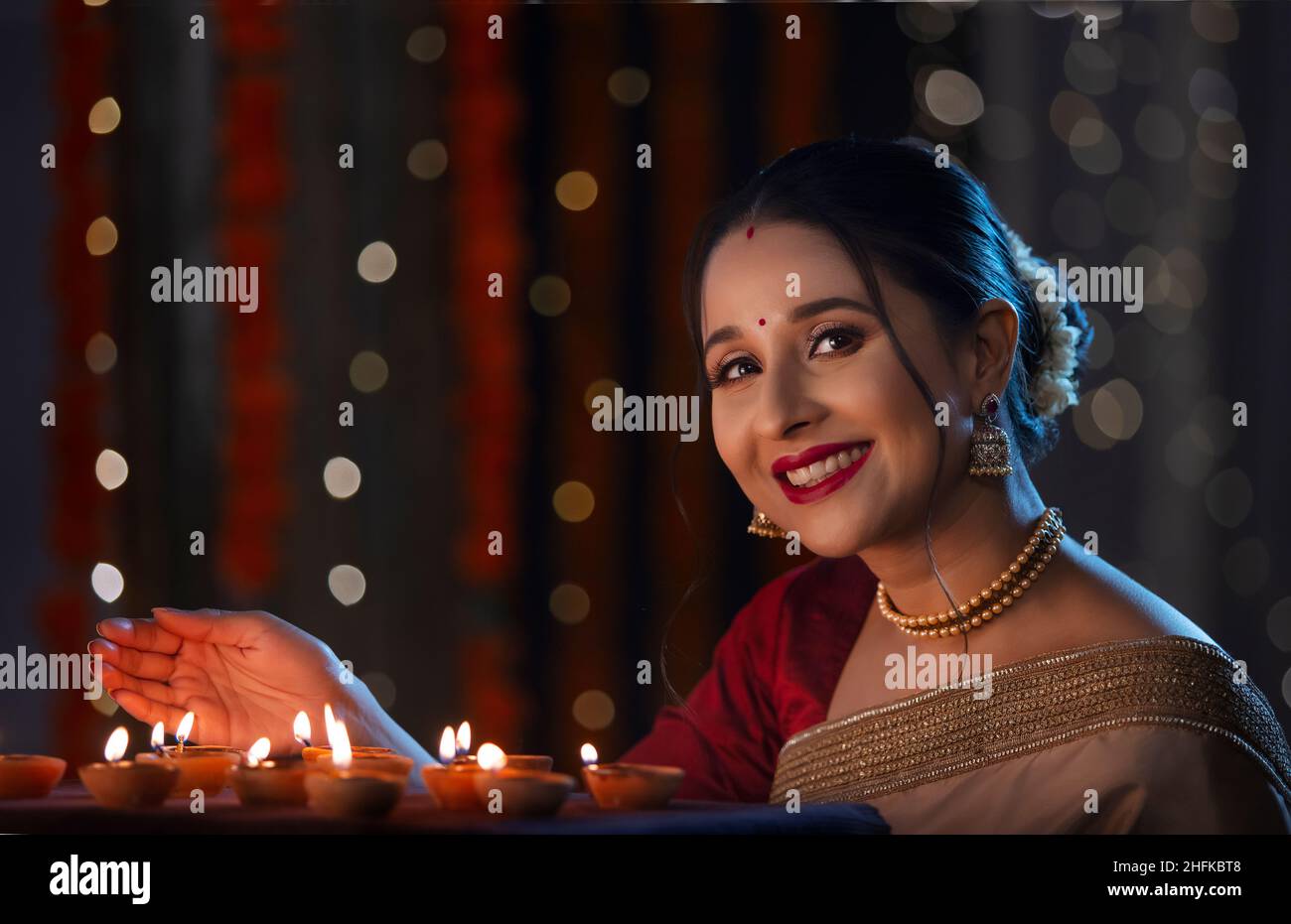 Indian beautiful lady posing in front of camera by covering the flame of diyas with hand on the occasion of Diwali Stock Photo