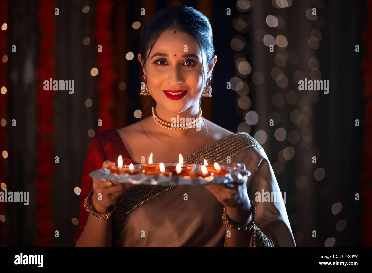 Indian beautiful woman posing with plate of diyas in front of camera on Diwali Stock Photo