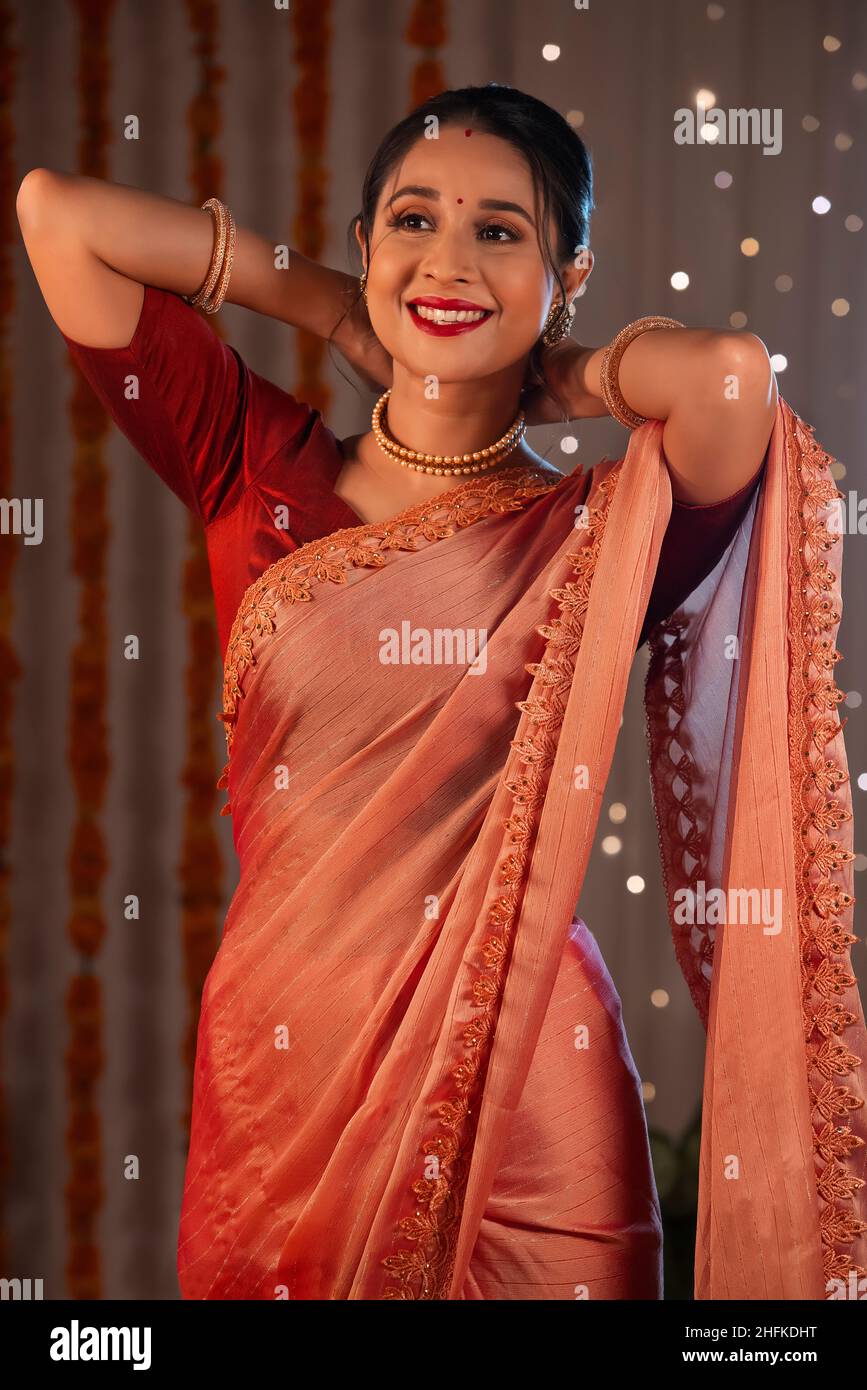 A beautiful woman standing while wearing a  pearl necklace and smiling amidst diwali decoration and lights. Stock Photo