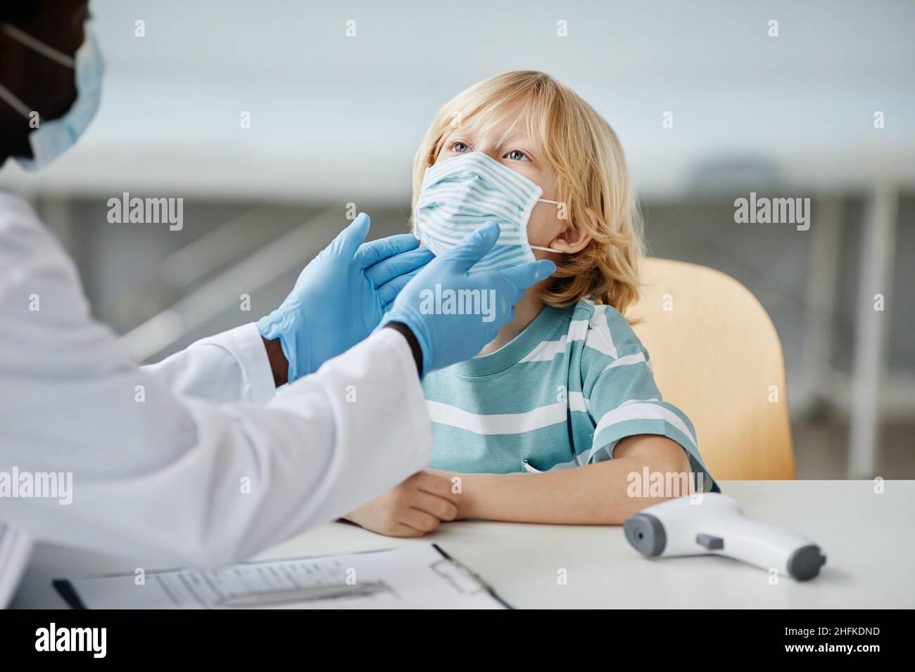 Unrecognizable doctor examining little boy wearing mask at child vaccination clinic, copy space Stock Photo