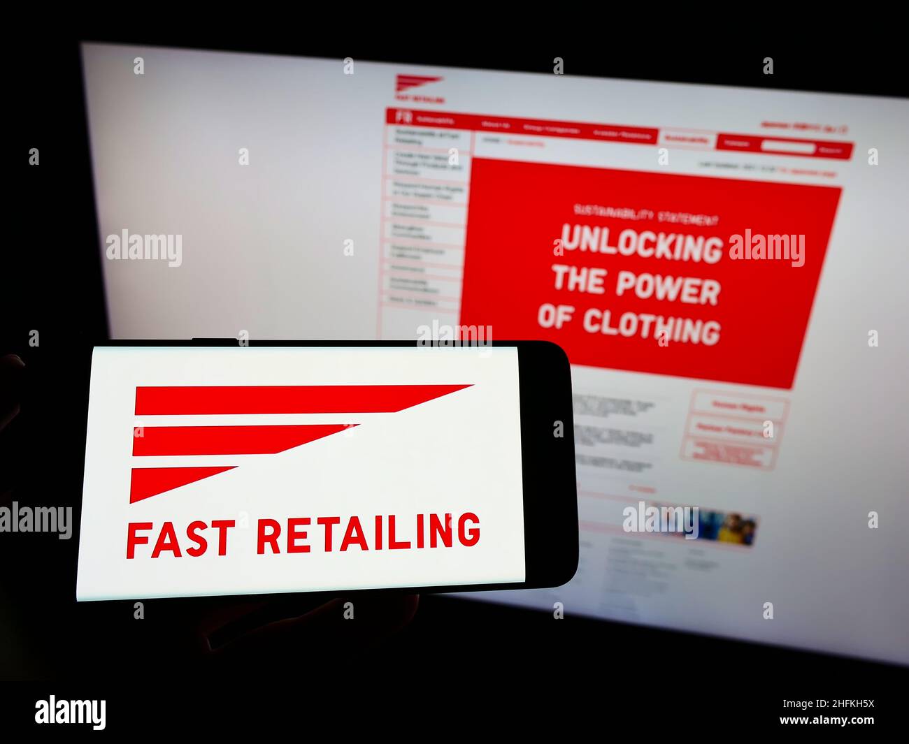 Person holding smartphone with logo of Japanese retail company K.K. Fast Retailing on screen in front of website. Focus on phone display. Stock Photo