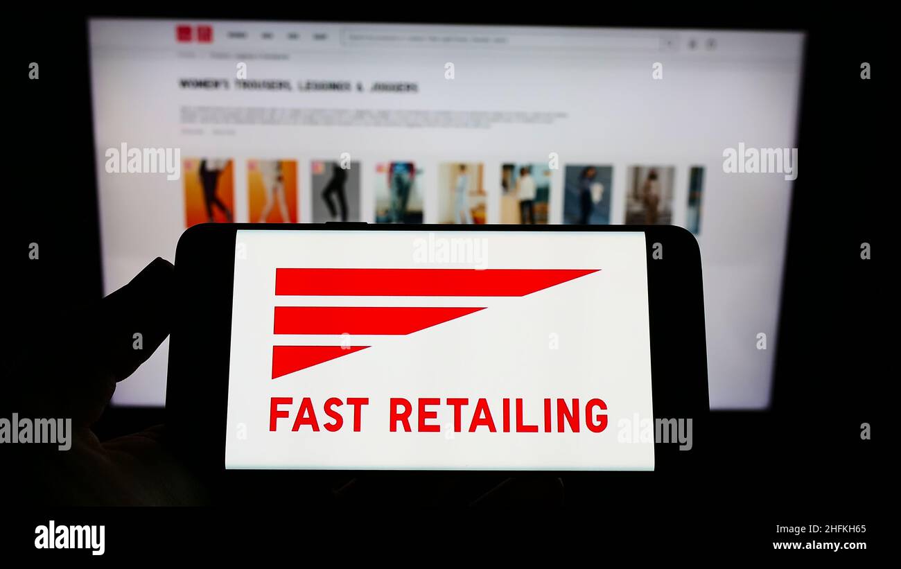 Person holding cellphone with logo of Japanese retail company K.K. Fast Retailing on screen in front of Uniqlo website. Focus on phone display. Stock Photo