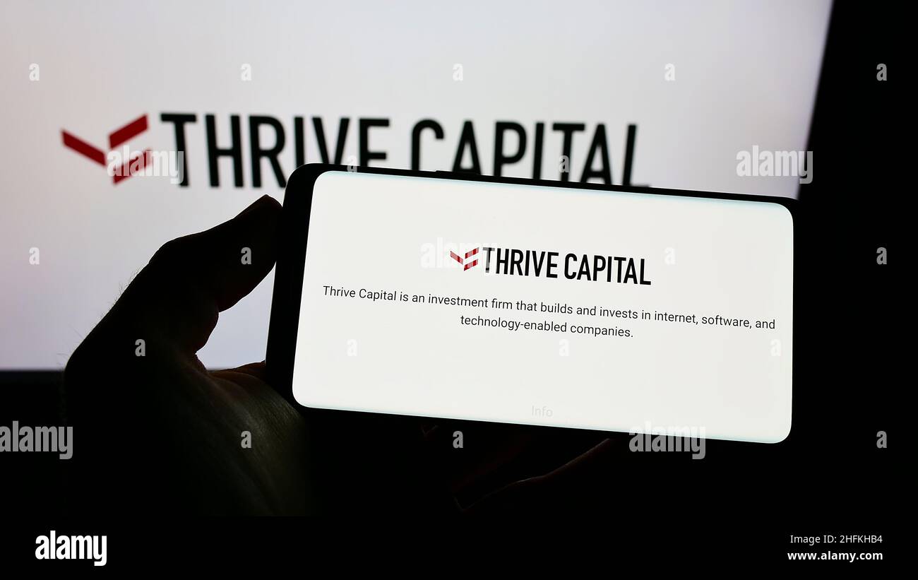 Person holding cellphone with website of US company Thrive Capital Management LLC on screen in front of logo. Focus on center of phone display. Stock Photo