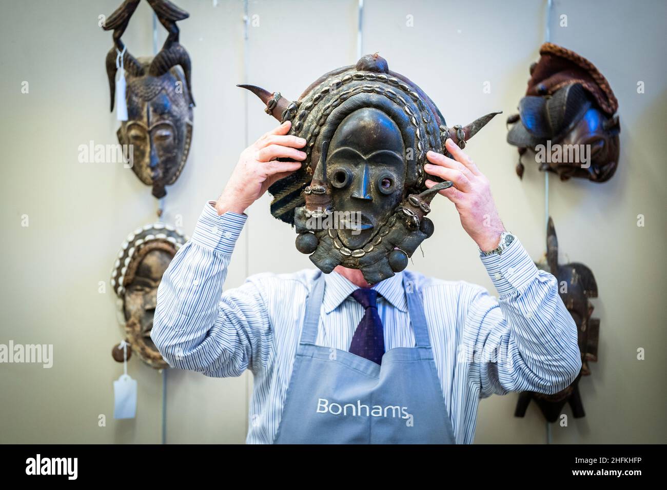 Bonhams' Danny McIlwraith holds a Nigerian polycrome carved wood mask during a photocall for the sale of the Jim Lennon Collection at Bonhams in Edinburgh. The collection of Silver, Asian and European Works of Art includes a rare Irish Neolithic bog oak dugout canoe, an 1877 Scottish silver Warwick vase by Mark Aitchison, a rare early English leaded bronze posnet dating from the 13th or 14th Century, and two pairs of Sancai glazed Guardian Figures from the Ming Dynasty. Picture date: Monday January 17, 2022. Stock Photo