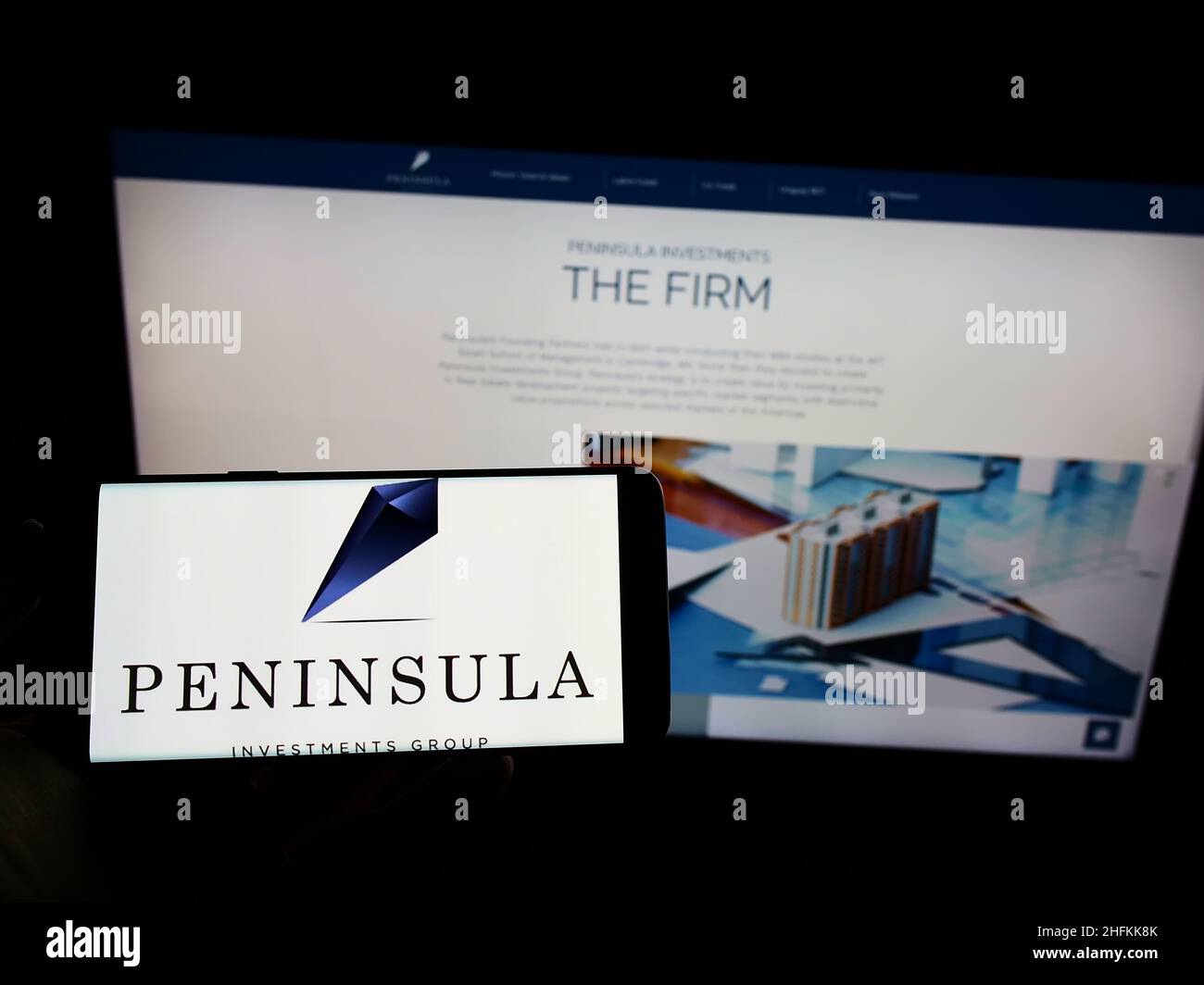 Person holding cellphone with logo of company Peninsula Investments Group Capital LLC on screen in front of webpage. Focus on phone display. Stock Photo