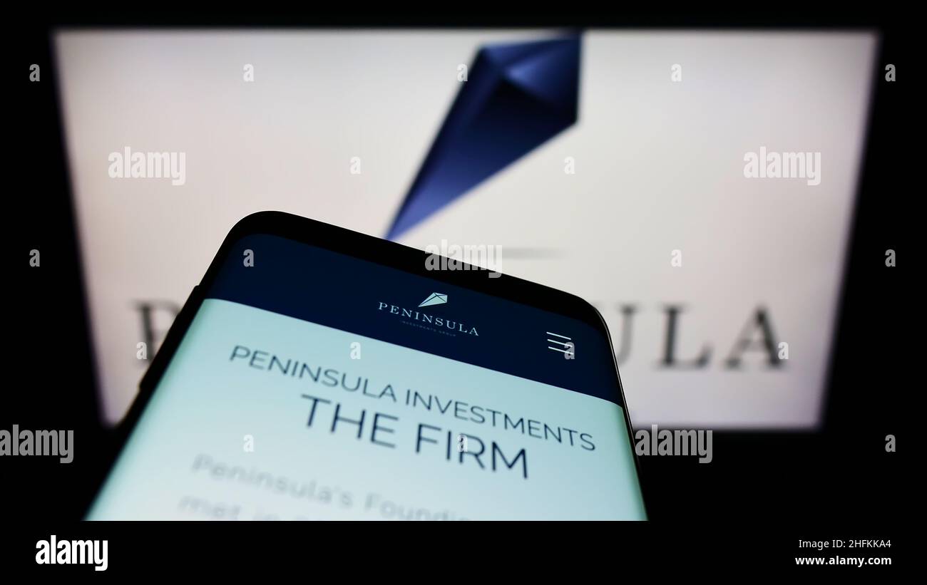 Mobile phone with webpage of company Peninsula Investments Group Capital LLC on screen in front of logo. Focus on top-left of phone display. Stock Photo