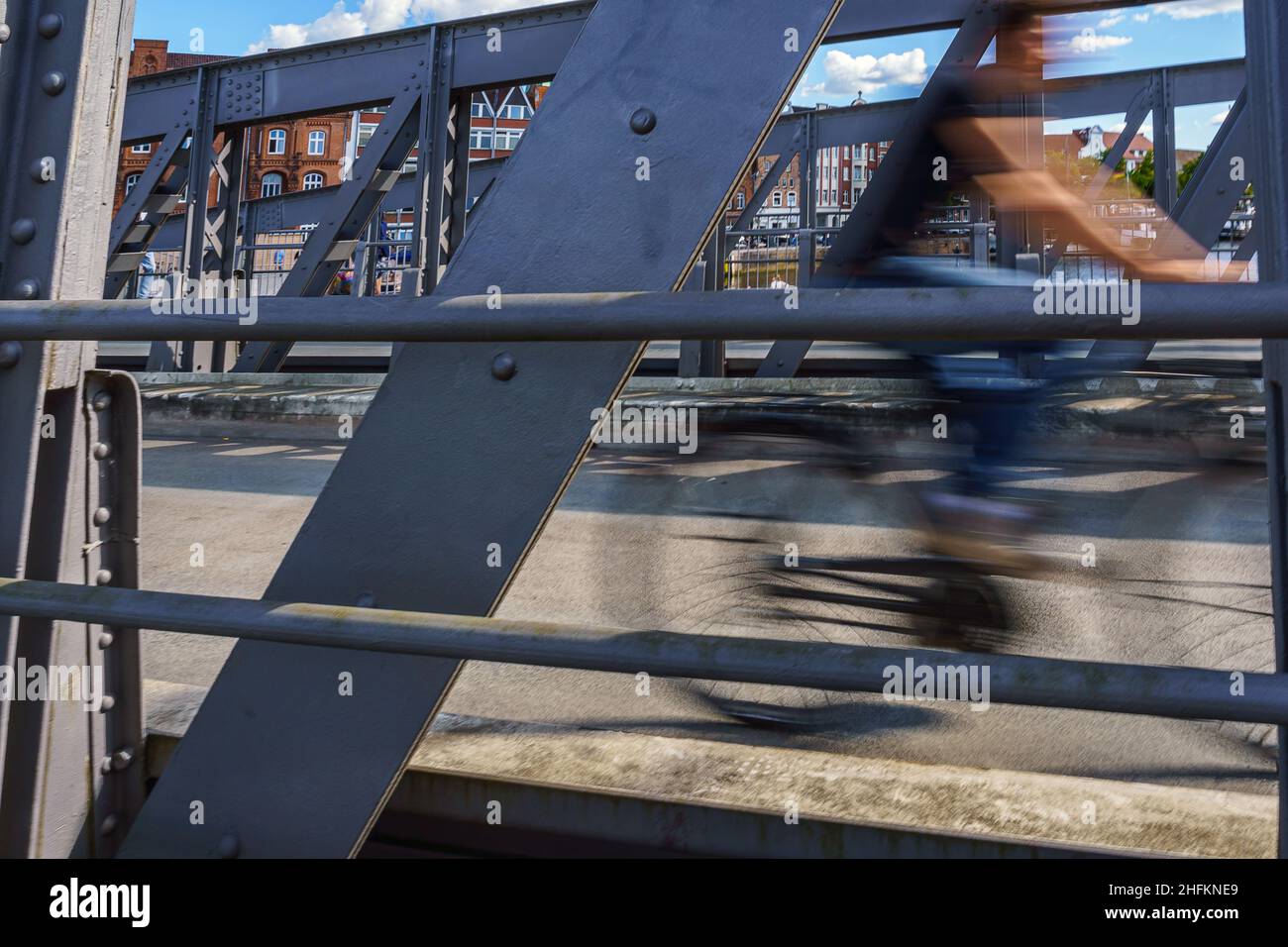 Eine junge Frau fährt mit ihrem Fahrrad über die Drehbrücke in Lübeck, sie ist nur verschwommen zu erkennen. Stock Photo