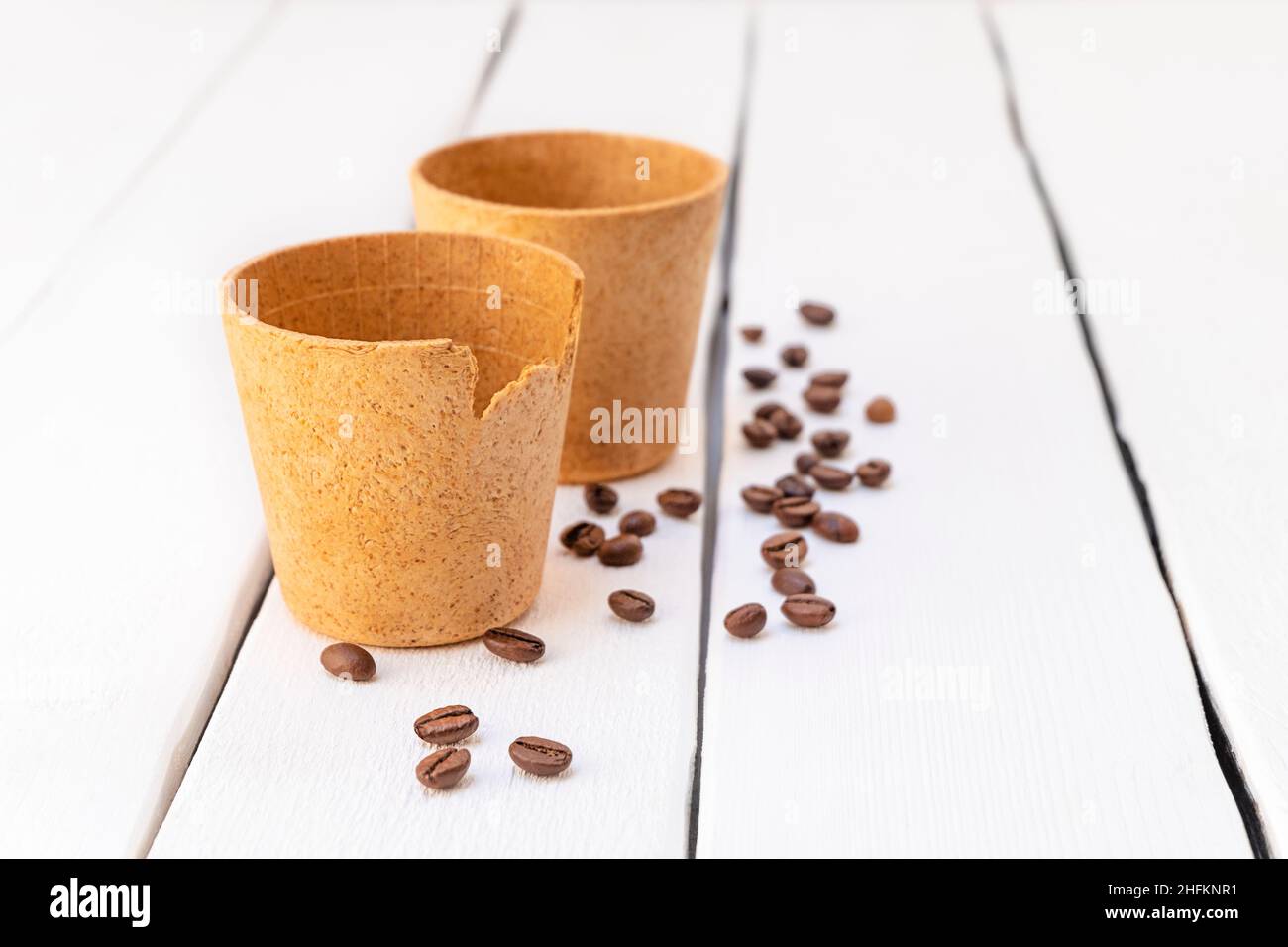 Eco-friendly waffle coffee cups with roasted coffee beans on white wooden table Stock Photo
