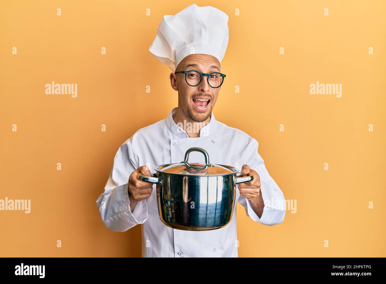 Bald man with beard wearing professional cook holding cooking pot celebrating crazy and amazed for success with open eyes screaming excited. Stock Photo