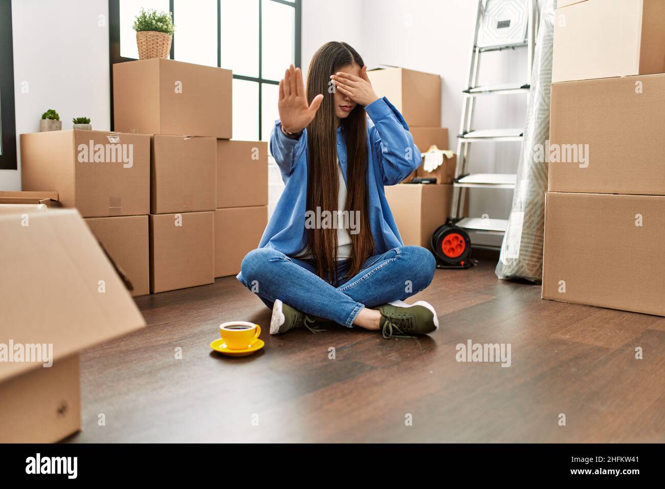 Young chinese girl sitting on the floor at new home covering eyes with ...