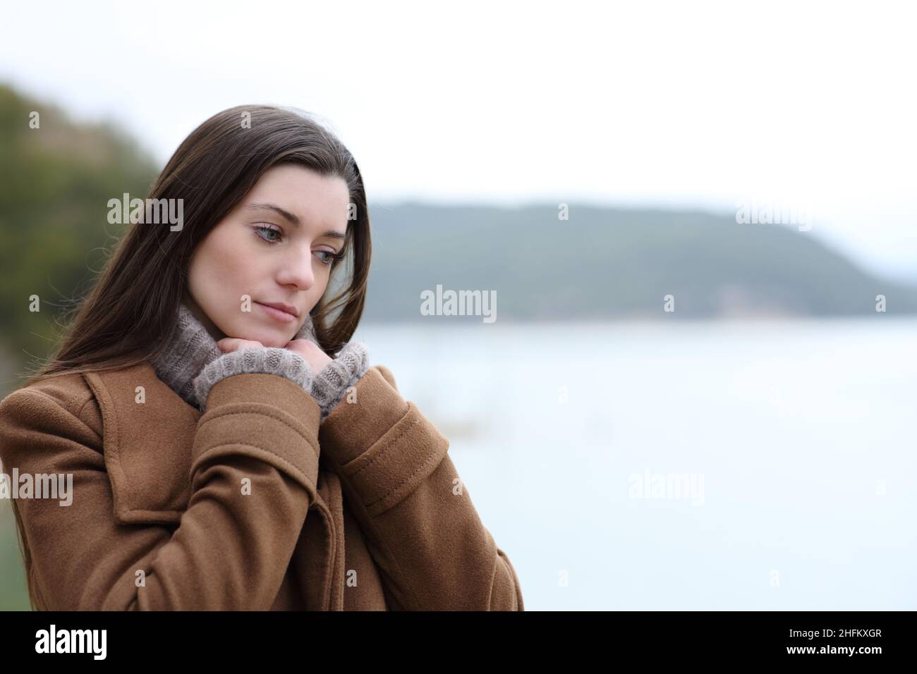 Pensive woman in winter thinking in a lake looking down Stock Photo