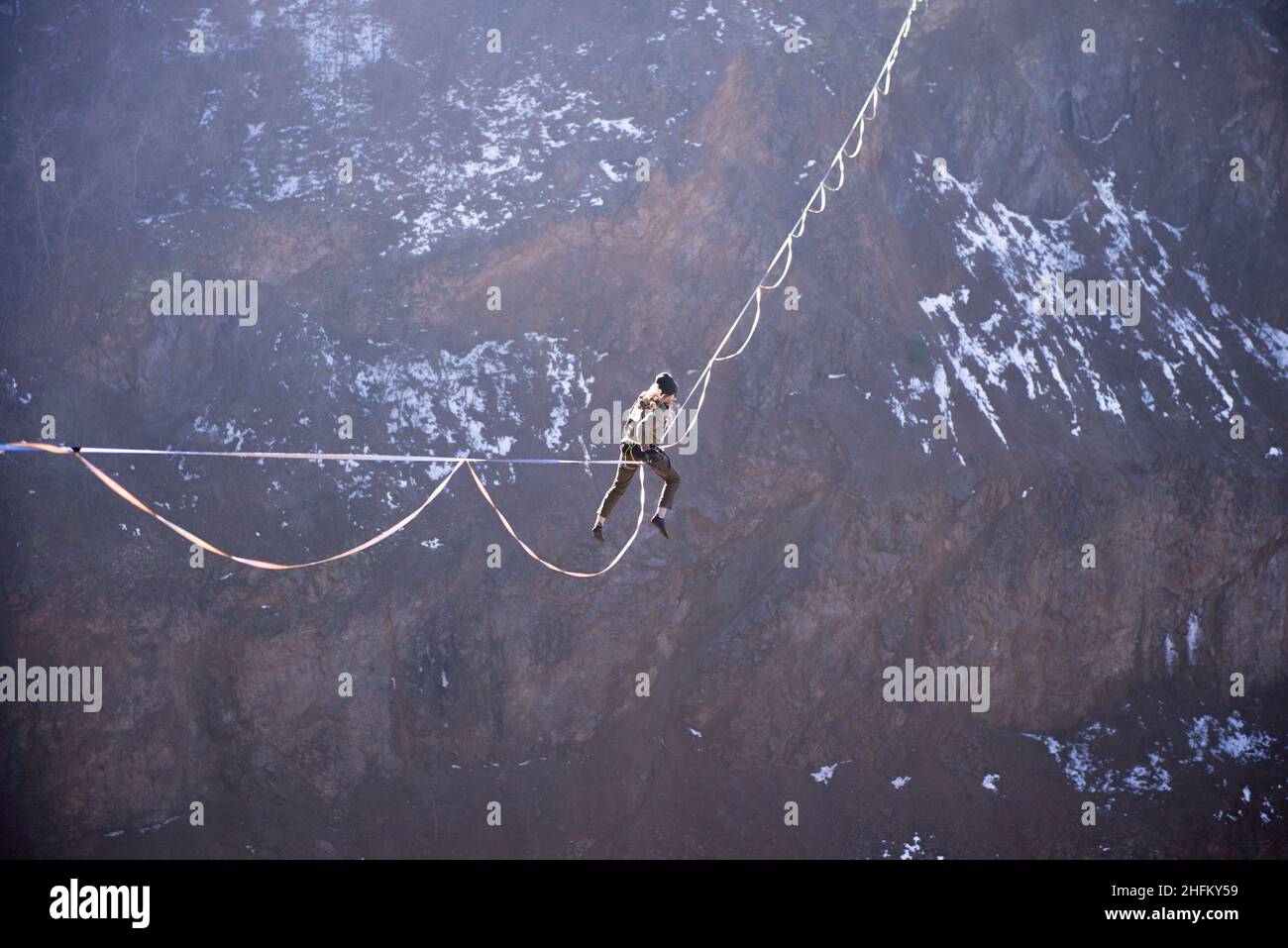 An athlete climbing to a highline to gain a foothold high over a beautiful lake Stock Photo