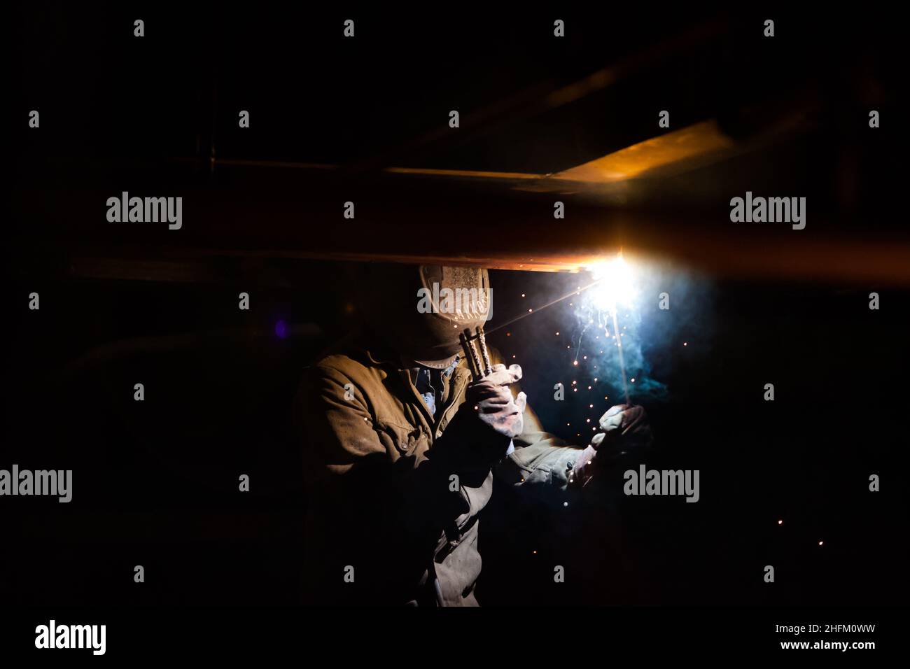 Welding of metal. Worker in mask and gloves. Bright light and sparks. Black background. Stock Photo