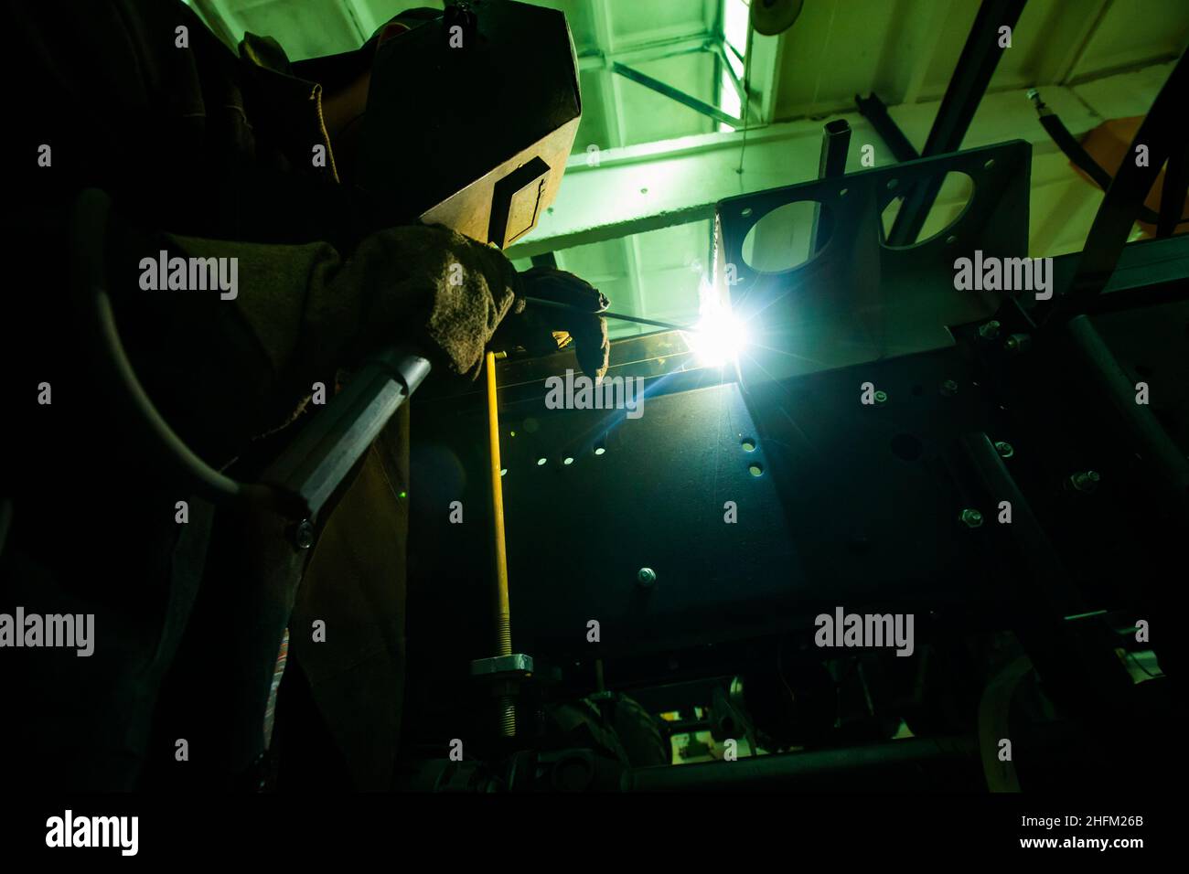 Welder in protective mask on green light welding metal part. Stock Photo