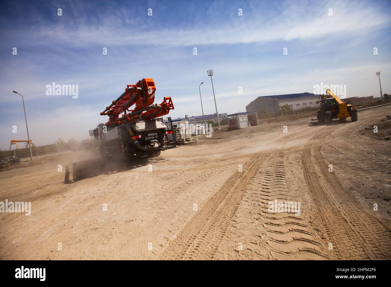 Two mobile cranes on desert dusty road. Truck tracks on foreground. Blue sky, clouds background. Stock Photo