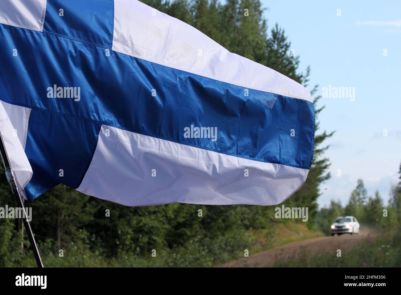 The detail of the Finnish flag waving in the wind taken during the Rally Finland. The racing car is in the background. Stock Photo