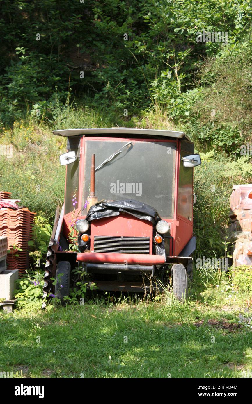 The abandoned wreck of a homemade tractor standing in the garden, overgrown with plants. Stock Photo