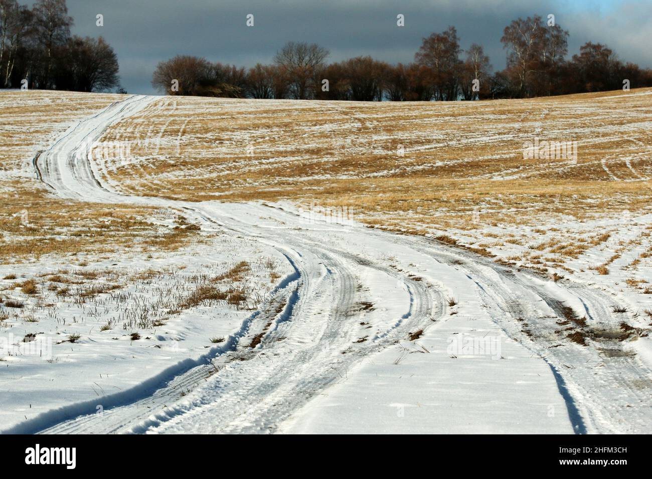 The empty field road heading in the curves to the horizon. Pictured during the winter season, covered by snow. Stock Photo