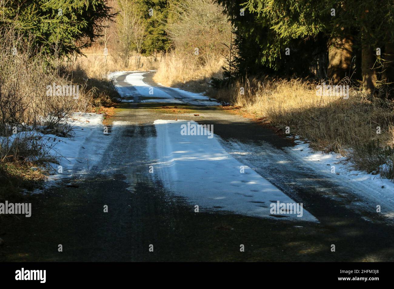 The detail of the narrow road in winter with risky driving conditions on snow and ice or black ice hiding in the shadows. Stock Photo