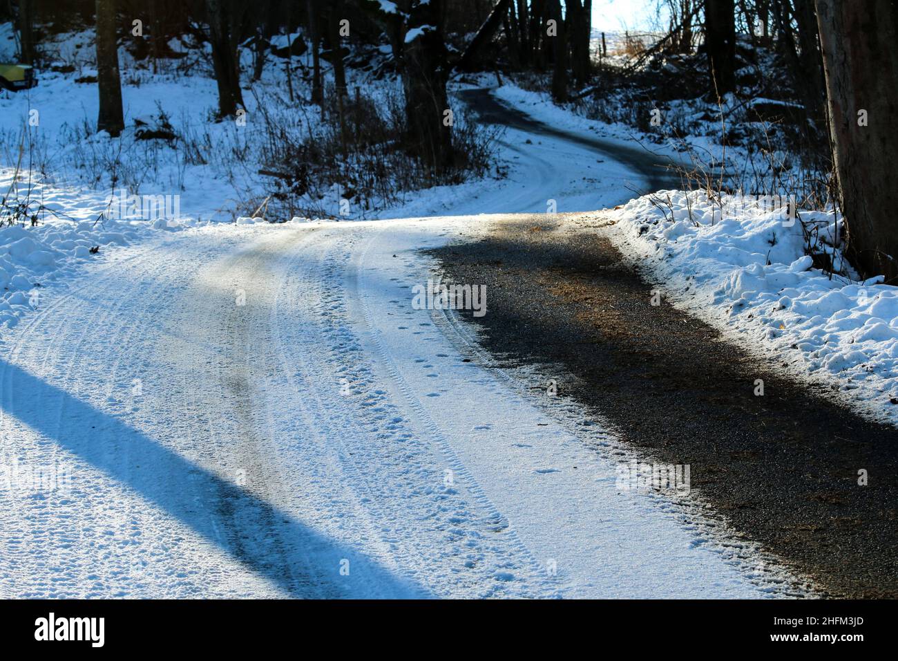 The detail of the narrow road in winter with risky driving conditions on snow and ice or black ice hiding in the shadows. Stock Photo