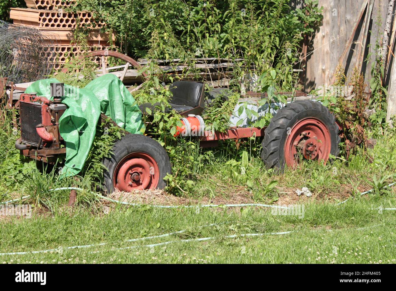 The abandoned wreck of a homemade tractor standing in the garden, overgrown with plants. Stock Photo