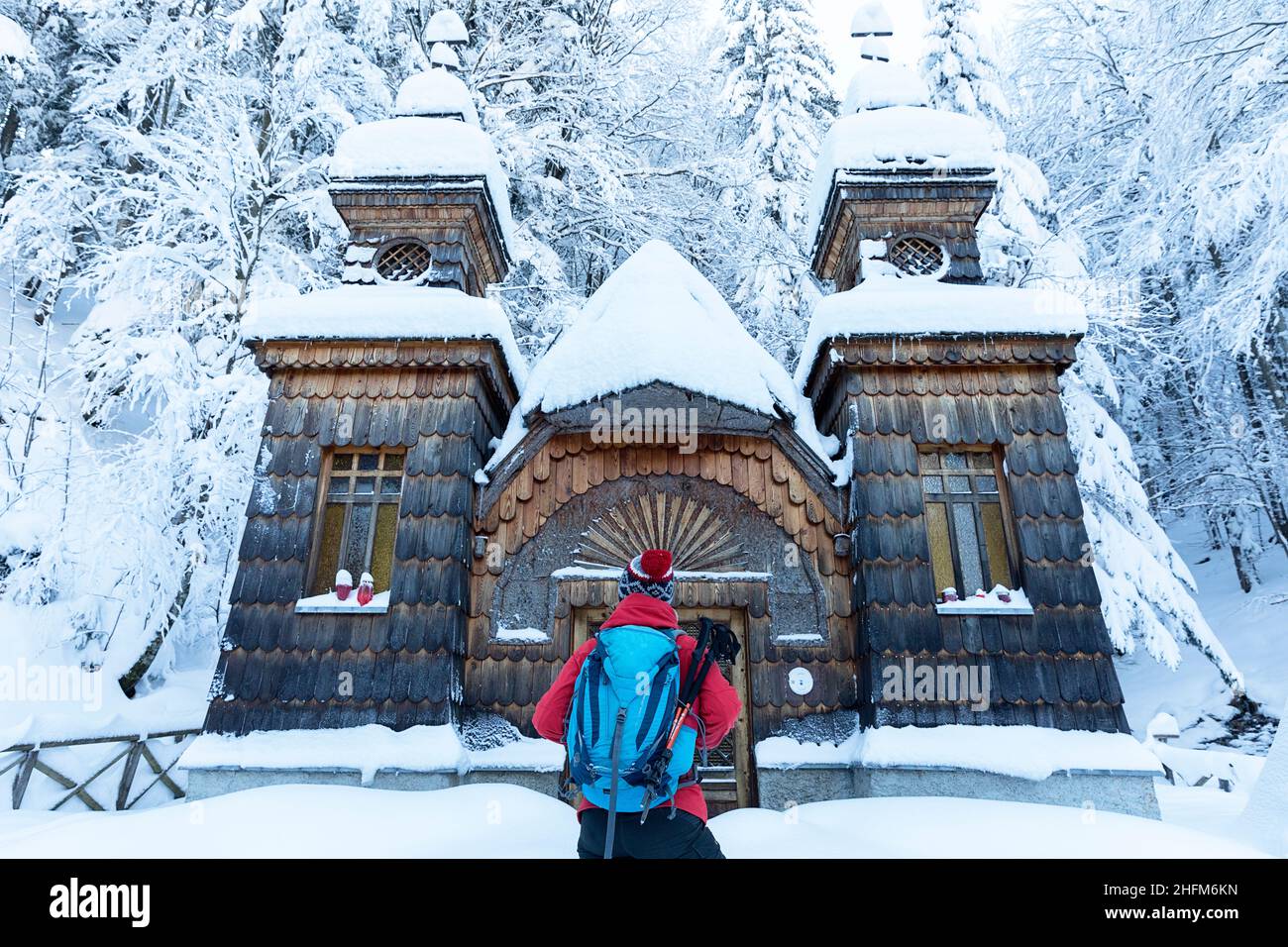 REar view of Woman in winter clothing and with a backpack standing in front of Russian Chapel on the Vršič Pass covered in snow, Julian Alps, Slovenia Stock Photo