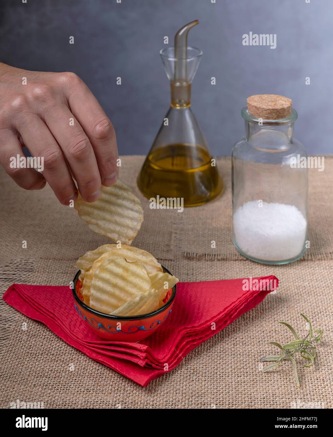 A male hand takes a potato chip from an orange saucer with salt and olive oil nearby Stock Photo