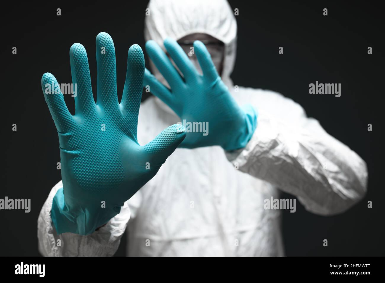 Medical professional dressed in full protective coverall clothing gesturing stop sign with hands in front of covid-19 red zone, selective focus Stock Photo