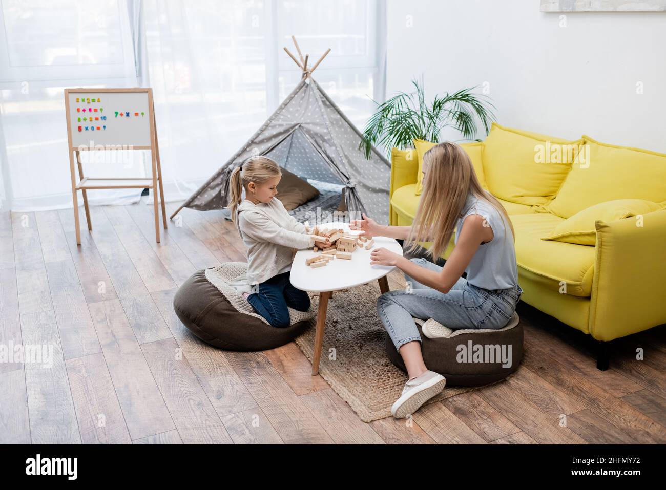 Child and mother playing wood blocks game near couch and teepee at home Stock Photo