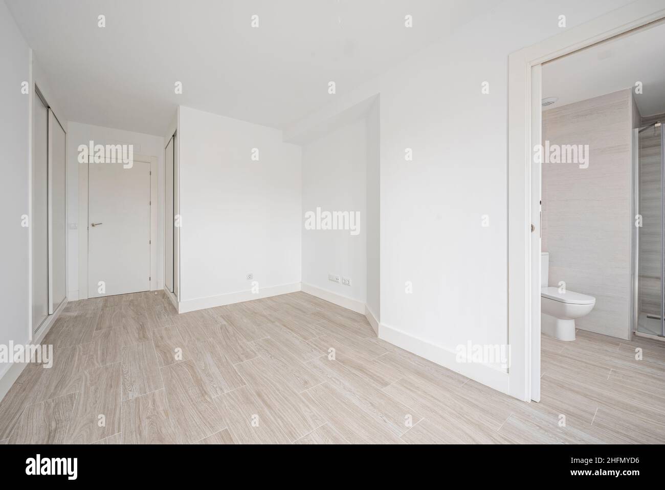 Empty room with white fitted wardrobes, white walls and wood-like ceramic tile floors and en-suite bathroom Stock Photo