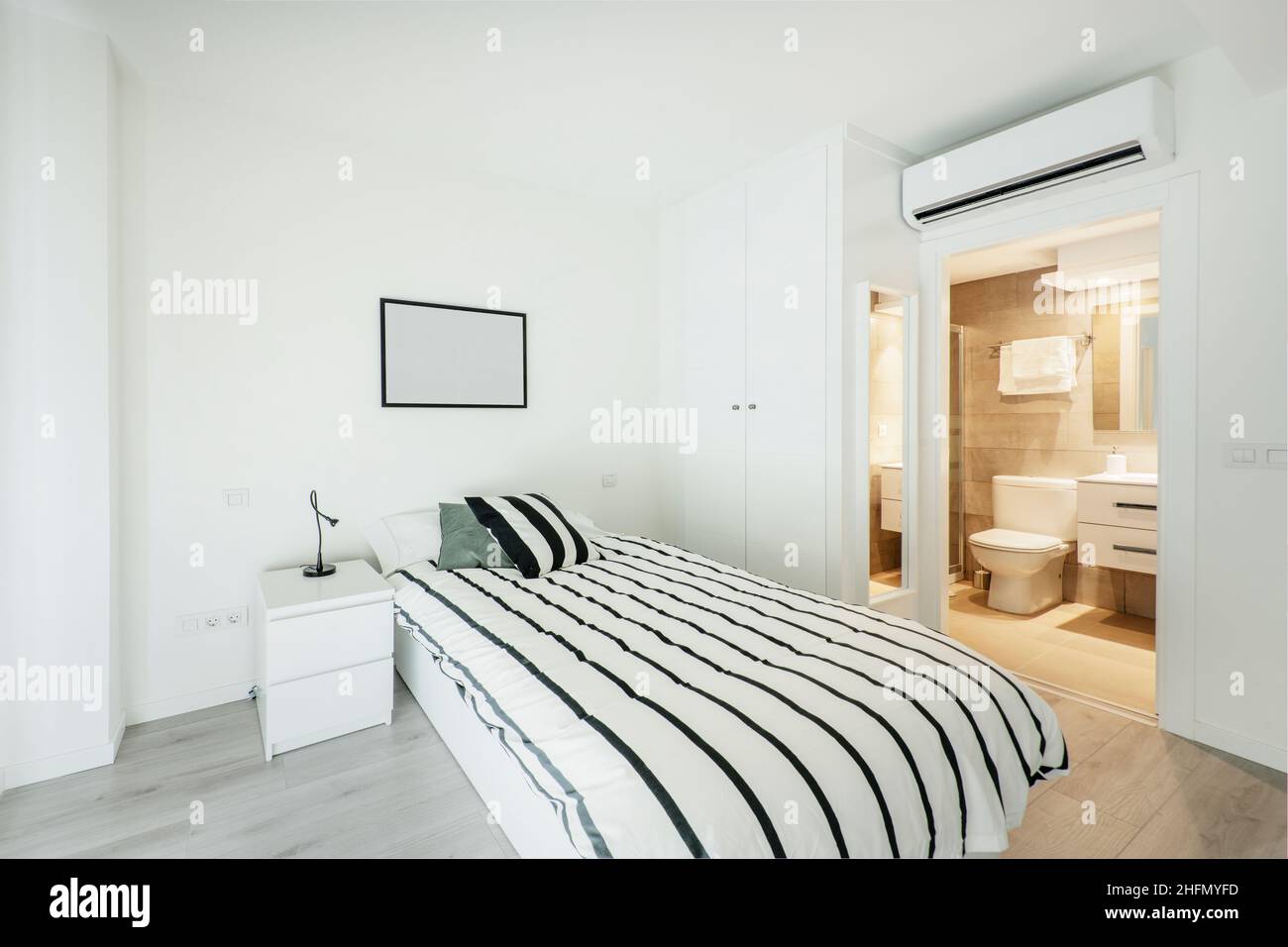 Bedroom with white walls and furniture with small bed, air conditioner and individual bathroom Stock Photo