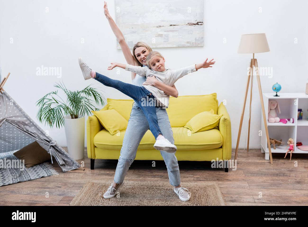 Happy woman holding child near couch and teepee at home Stock Photo