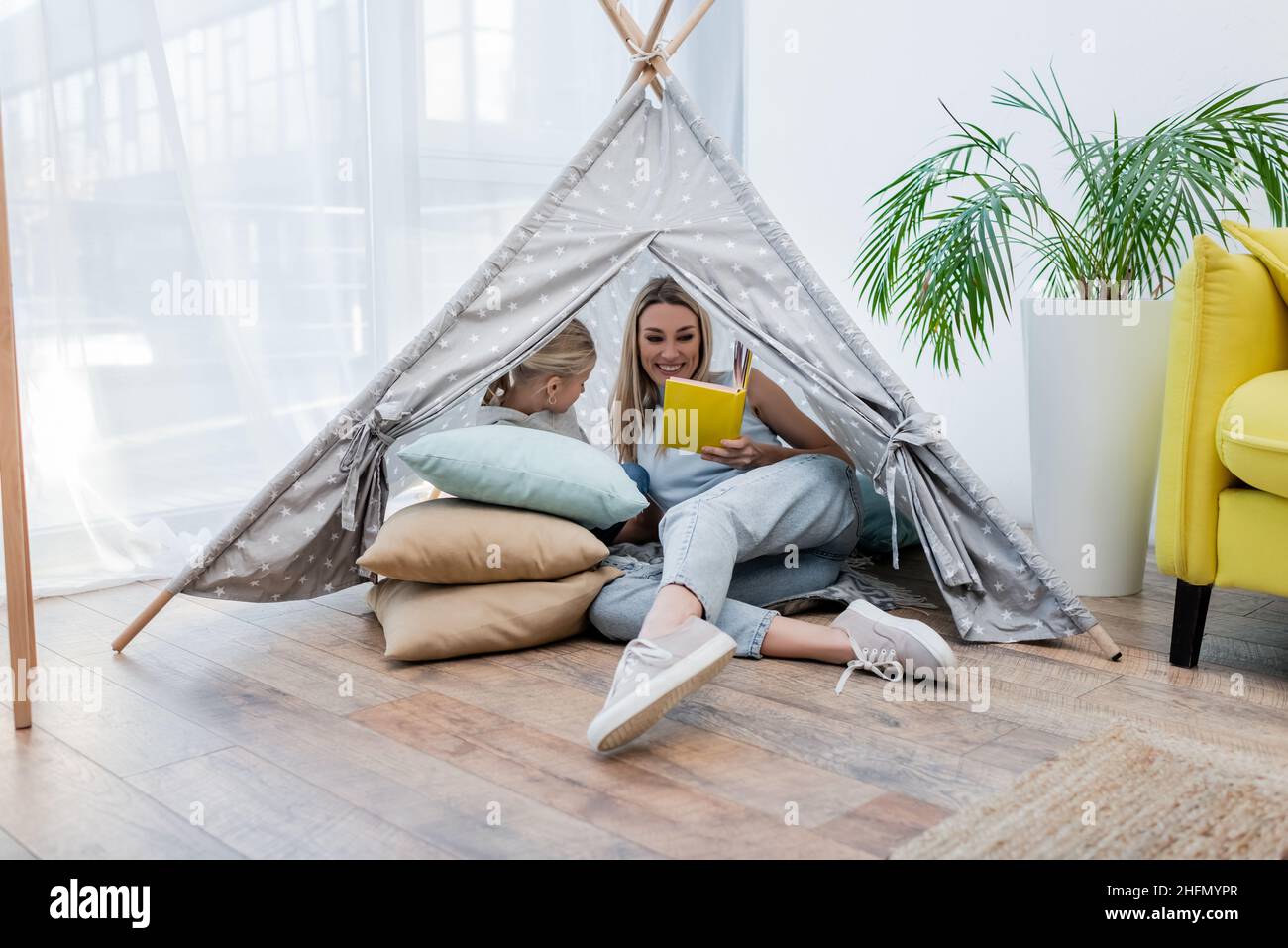 Mother reading book near child in teepee at home Stock Photo