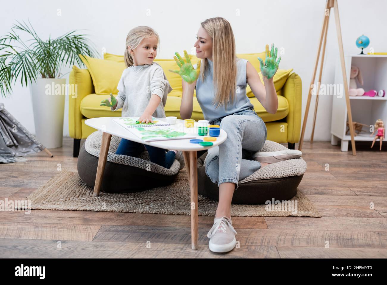 Kid with paint on hands looking at mother near coffee table at home Stock Photo