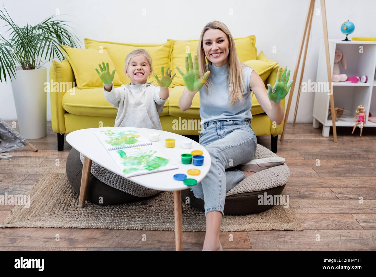 Smiling mother and child looking at camera while showing hands in paint at home Stock Photo
