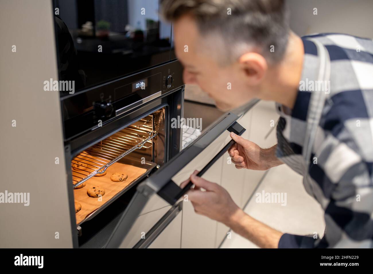 Man looking into open oven at baking cookie Stock Photo Alamy