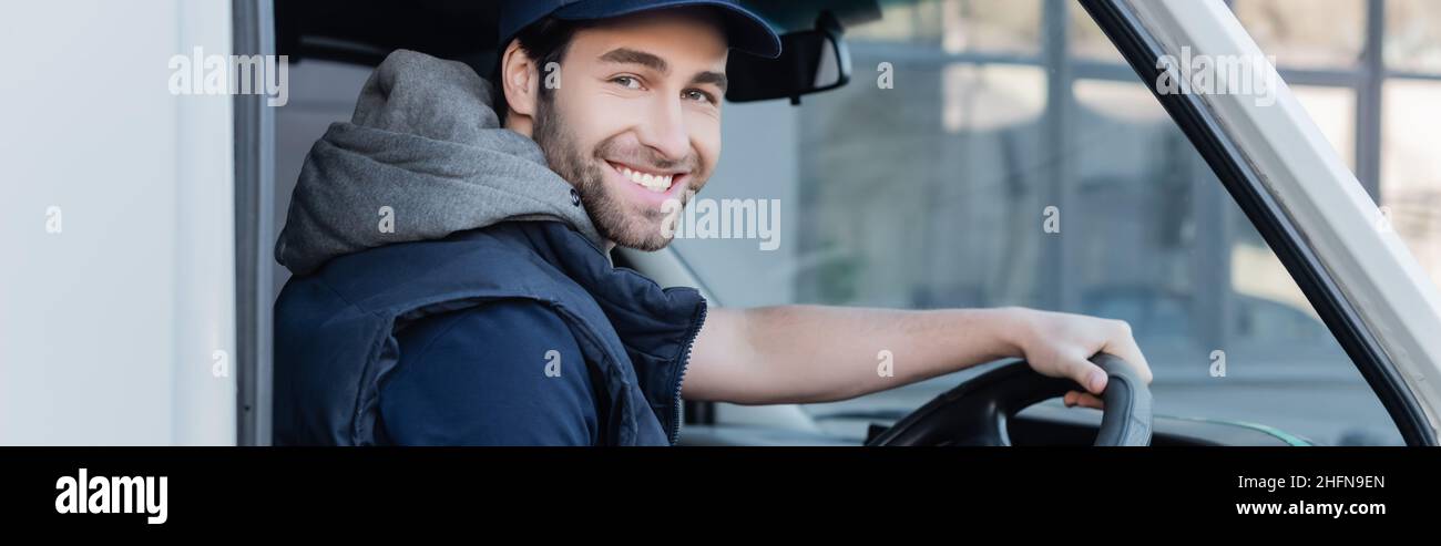 Positive delivery man smiling at camera while driving auto, banner ...