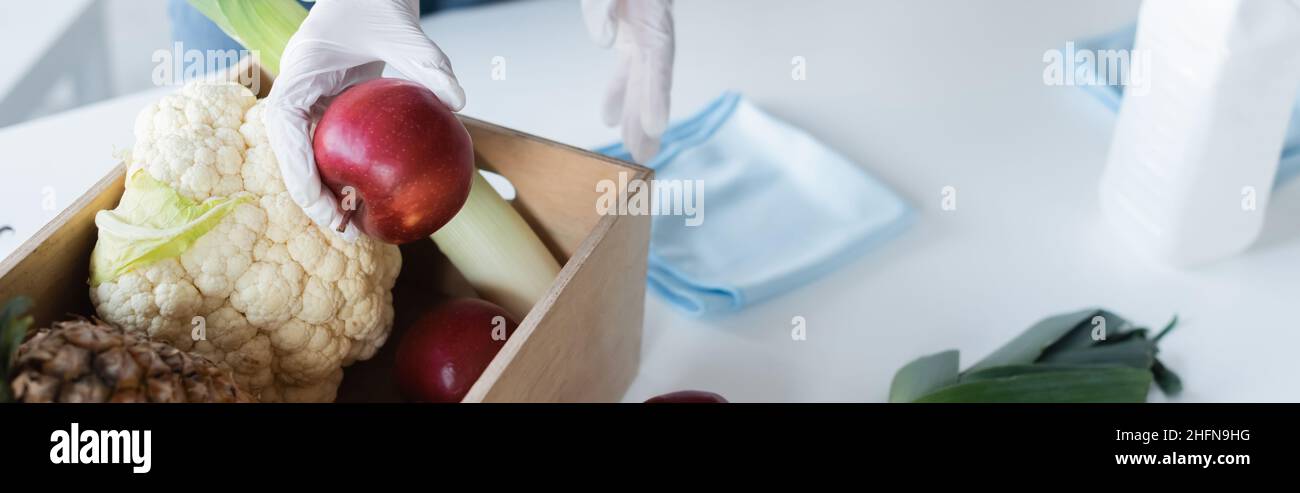 Cropped view of woman in latex gloves holding apple near food, rags and ...