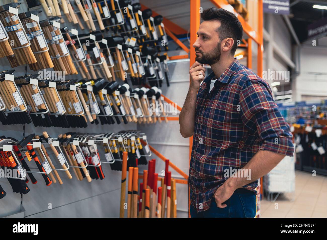 a man next to a rack with hammers in a hardware store chooses a tool