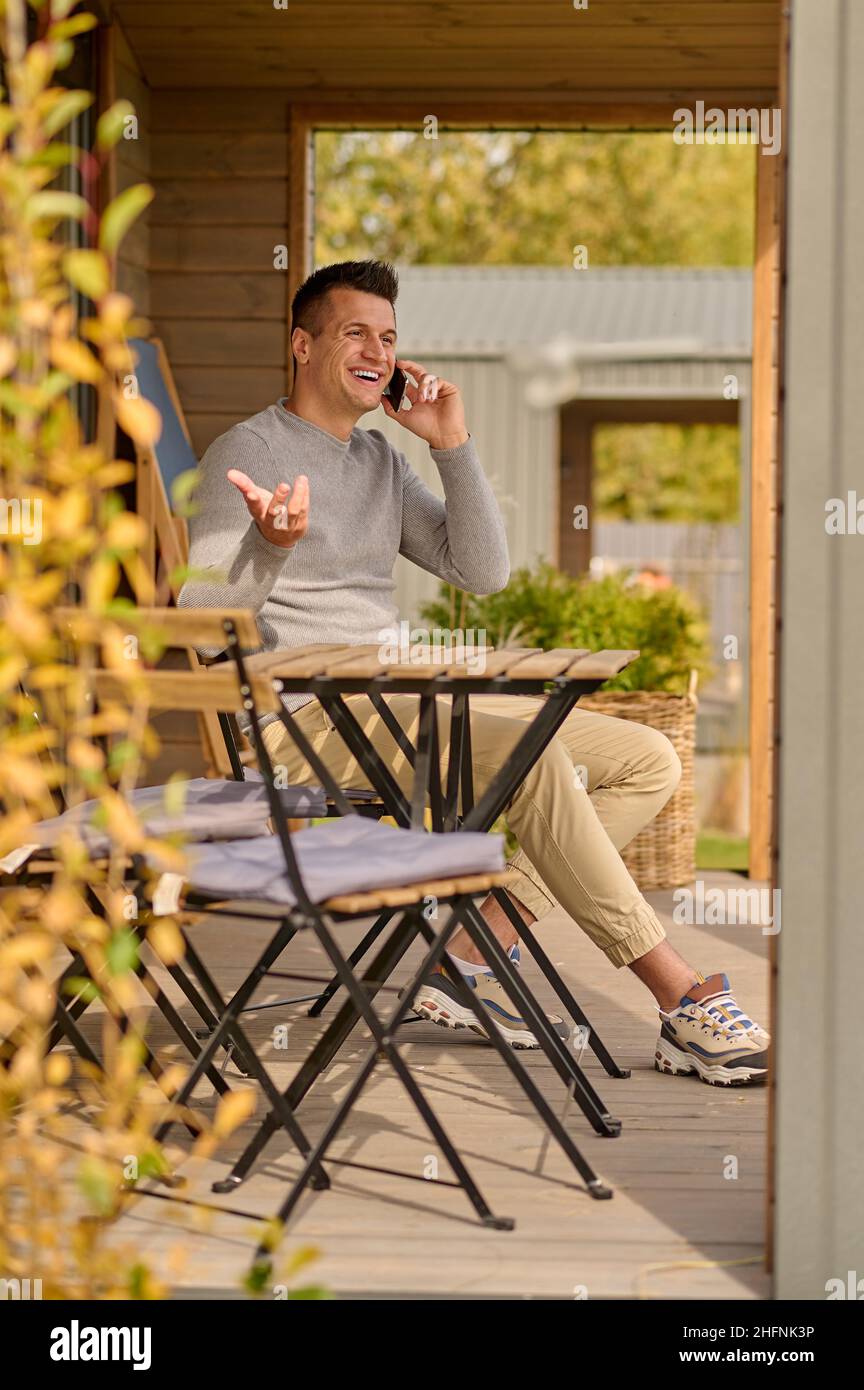 Man talking on smartphone gesturing sitting outdoors Stock Photo
