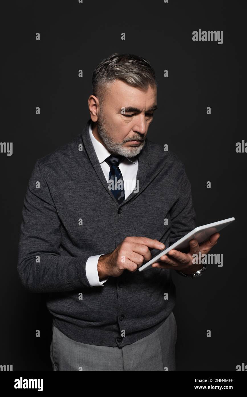 grey-haired man in stylish clothes using digital tablet on dark grey Stock Photo