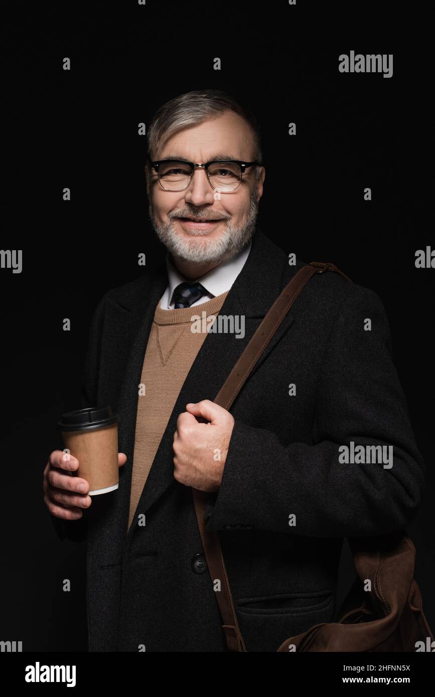 positive bearded man with leather bag and glass of whiskey looking at camera isolated on black Stock Photo