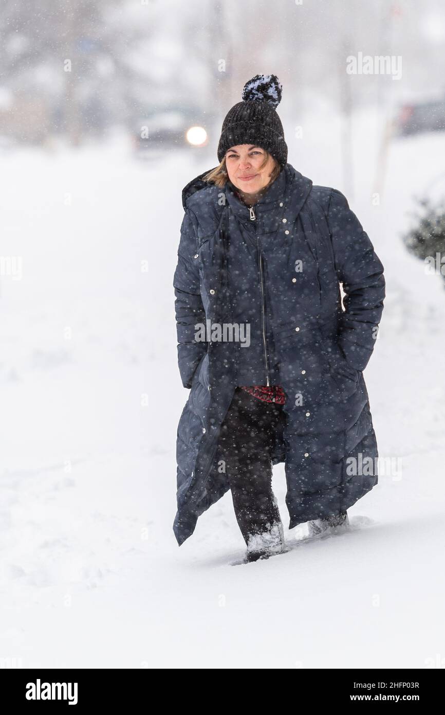 A Latin American woman braving the Canadian Winter. She walks on an uncleared sidewalk full of snow. The Winter snowstorm has caused many disruptions Stock Photo