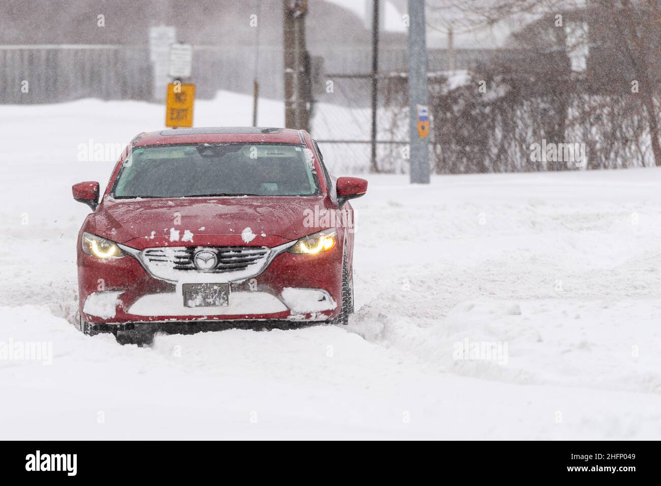A red Mazda car turns from the snow-cleared Victoria Park Avenue towards the uncleared Terraview Blvd.  during a Winter snowstorm in Toronto, Canada Stock Photo