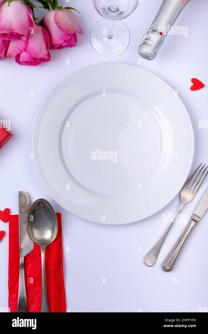 Empty white plate surrounded by pink roses with bottle and cutlery on table Stock Photo