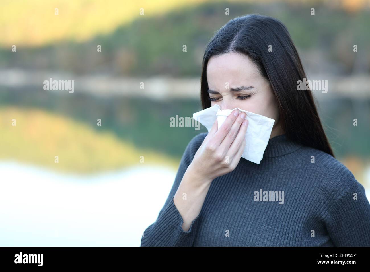 Ill woman blowing nose with a tissue outdoors in winter Stock Photo