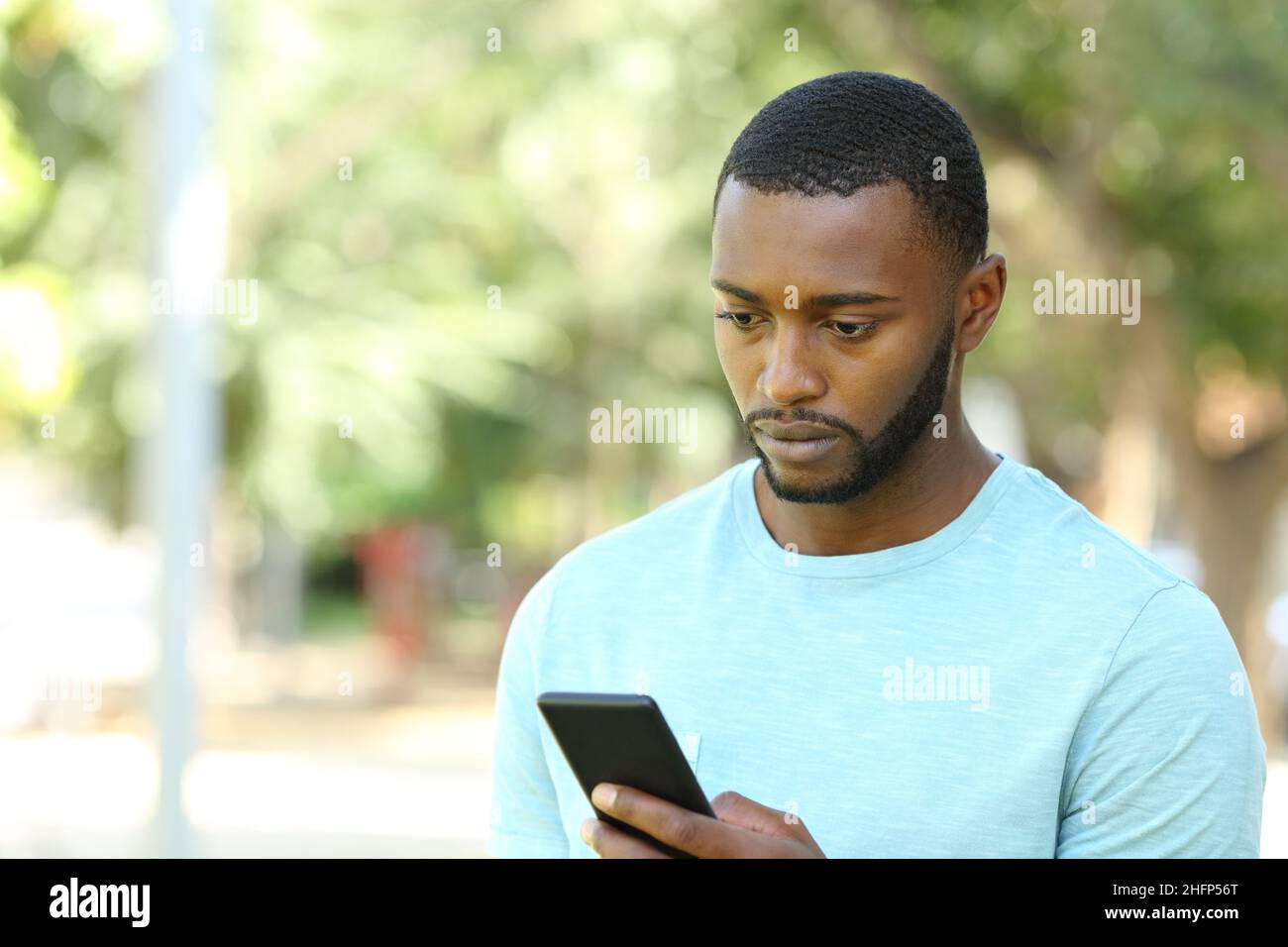 Worried man with black skin checking mobile phone walking in a park Stock Photo