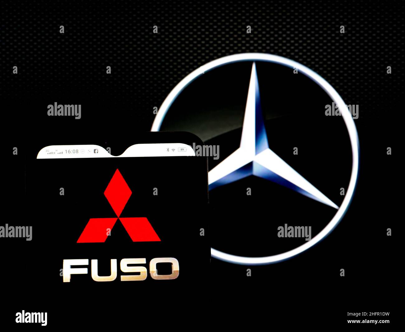 In this photo illustration, the Mitsubishi Fuso Truck and Bus Corporation logo is seen displayed on a smartphone screen with the Daimler AG logo in the background. Stock Photo